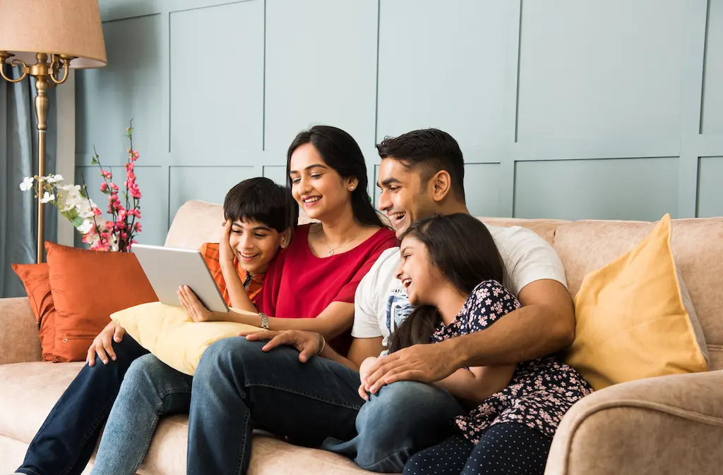 Family of four laughing on a sofa while looking at a tablet