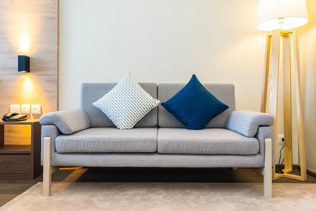 Modern grey loveseat with two accent cushions between a floor lamp and side table