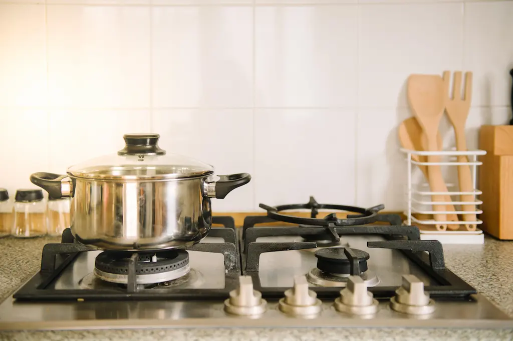 Stainless pot on gas cooktop with utensils in the background