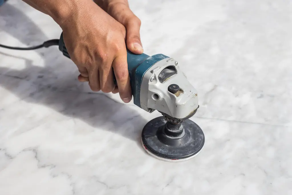 Handheld polisher buffing a marble floor close‑up