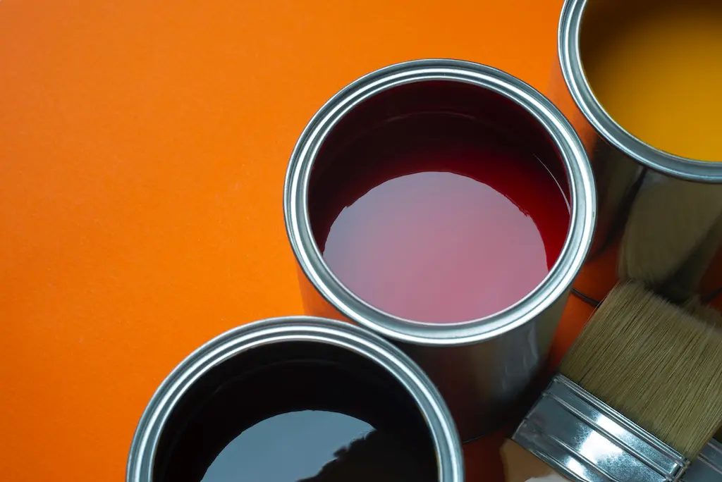 Open paint cans in black, red, and yellow with a brush on an orange background