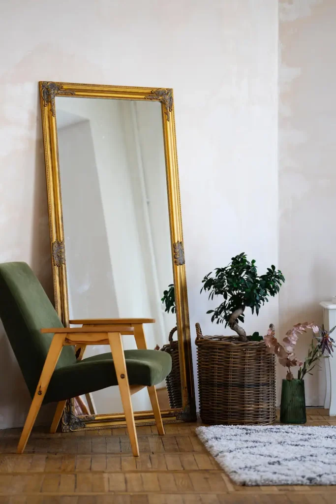 Vintage gold-framed floor mirror beside a green armchair and woven plant basket