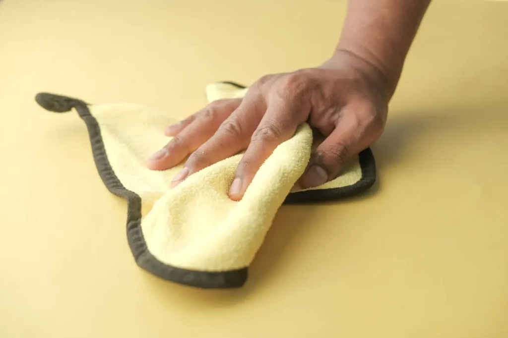 Hand wiping a surface with a yellow microfiber cloth.