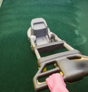 Person using a floor cleaning machine on green carpet.