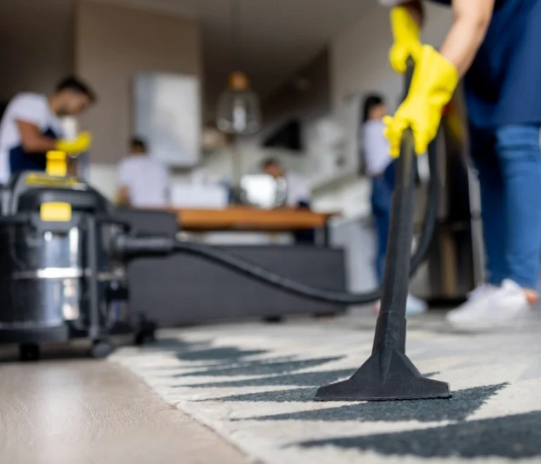 Person wearing yellow gloves vacuuming a patterned carpet in an office setting