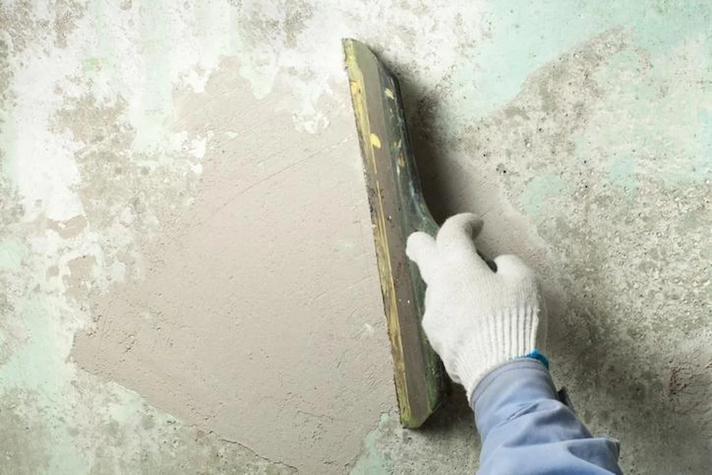Gloved hand smoothing wall surface with sandpaper or sanding tool.