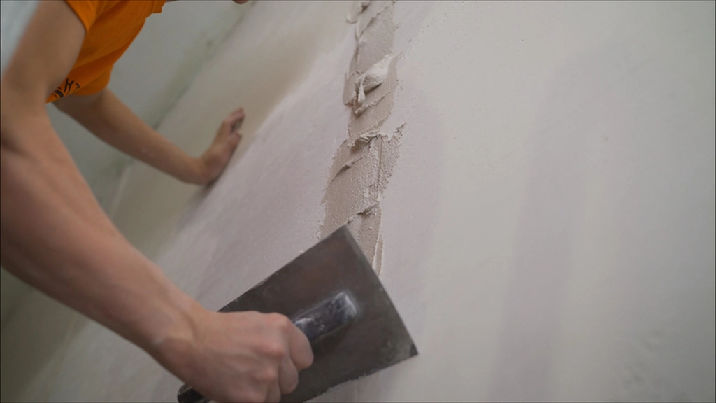 Person applying wall putty to repair cracks with a putty knife.