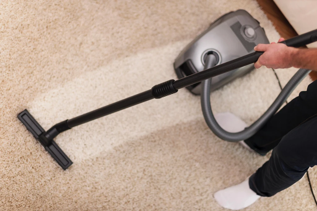 Person vacuuming a beige carpet, showing a clean path, by Clean Fanatics.