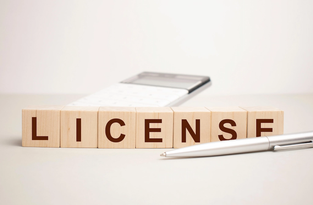 Wooden blocks spelling "LICENSE" with a pen and notepad