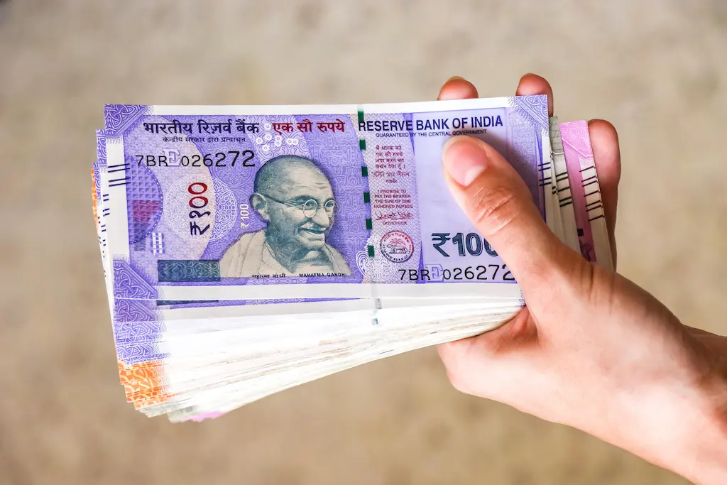 Hand holding ₹100 notes in a money stack -cleanfanatics