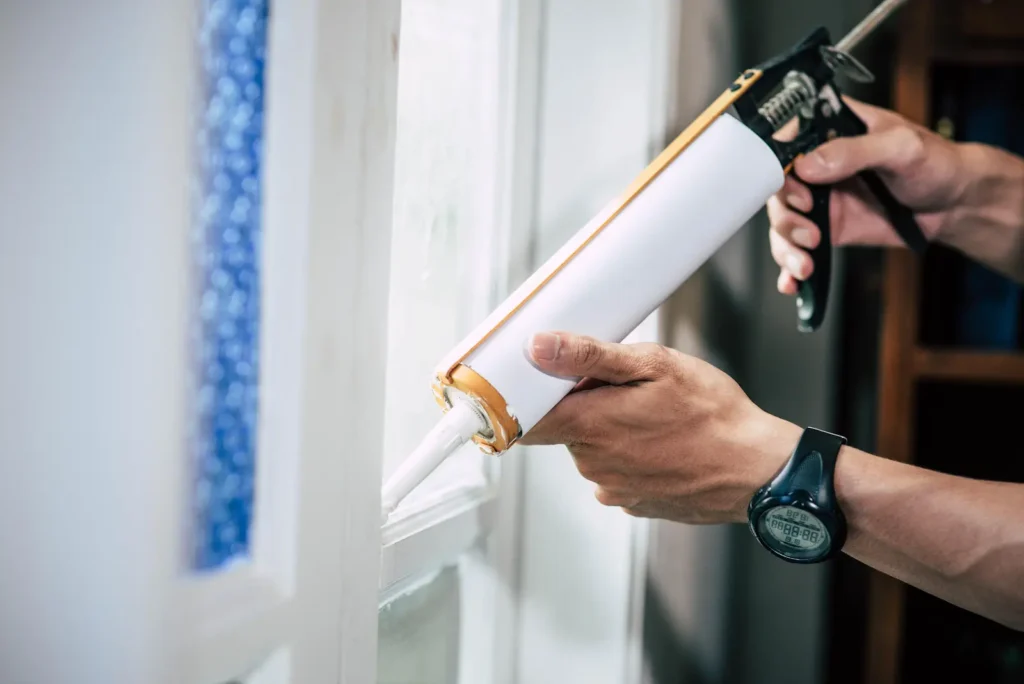 Hand applying caulk with a caulking gun to seal a window frame.